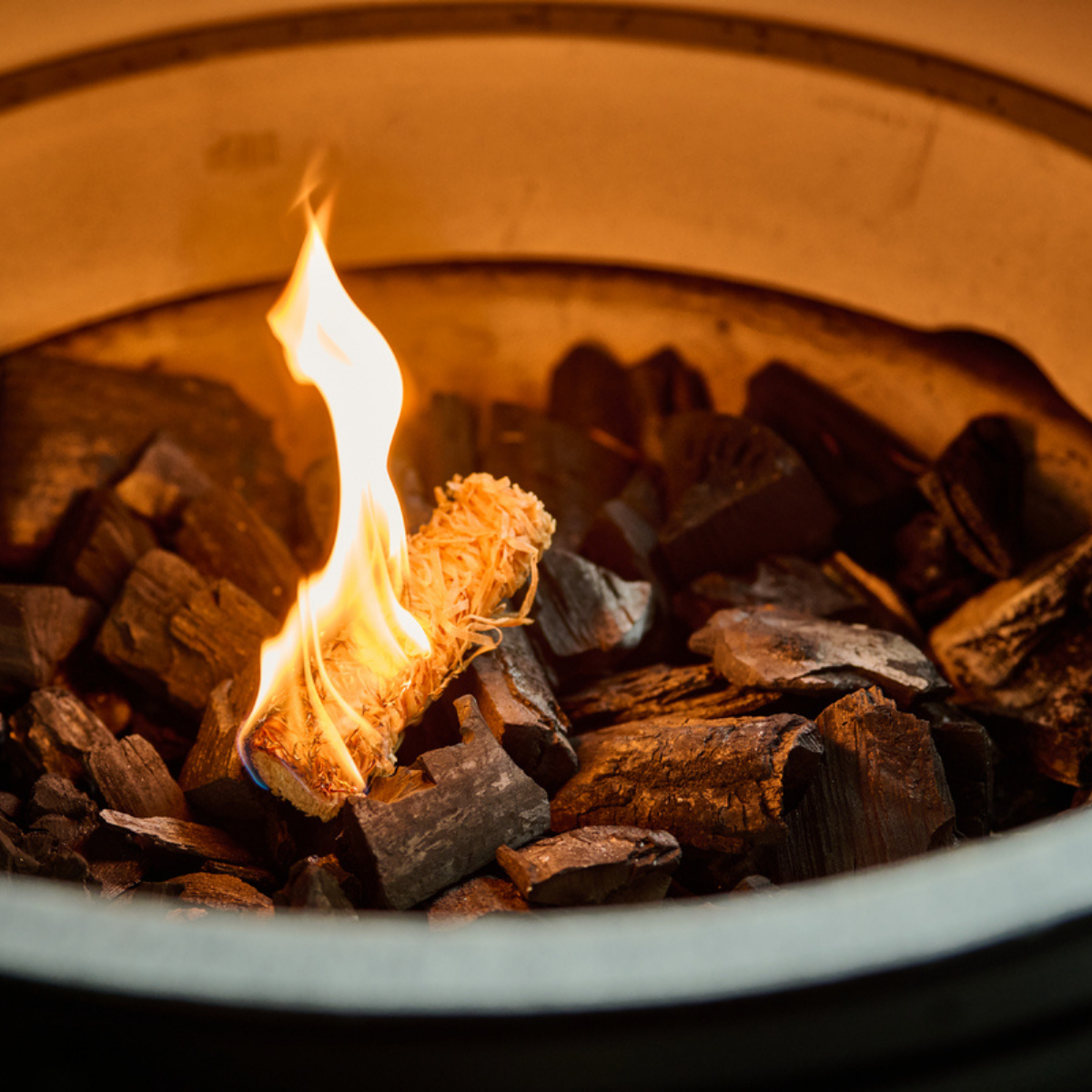 A close-up view of Big Green Egg Twister Firestarter stick lit on charcoal in the fire bowl of a Big Green Egg.