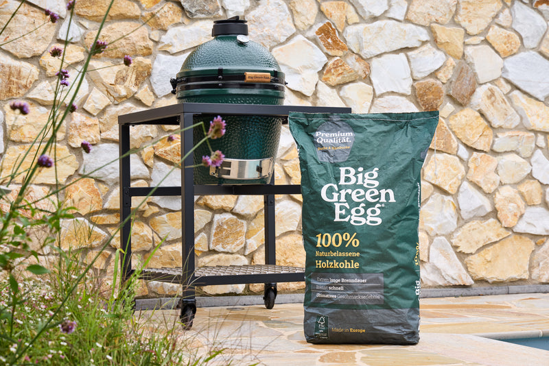 Ein Sack 100 % naturbelassene Holzkohle von Big Green Egg steht vor einem Holzkohlegrill aus Keramik
