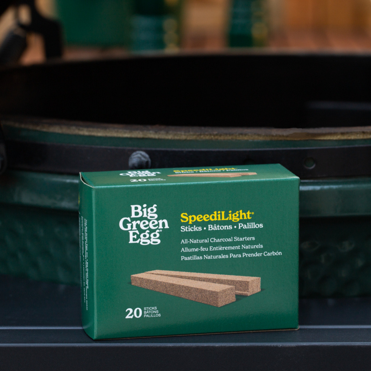 A box of Big Green Egg SpeediLight all-natural charcoal starter sticks, shown on a dark green ceramic grill burner.